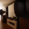 A high-end audio room featuring large Vista 3-Way Horn Speakers and a collection of tube amplifiers and preamplifiers on shelves, set in a dimly lit room with wooden floors.