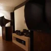A room featuring large, sculptural black Vista 3-Way Horn Speakers and a collection of audio equipment including a preamplifier on a wooden shelf.