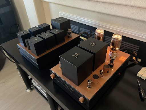 A GM70 Integrated Amplifier setup on a wooden desk featuring glowing tubes and several black electronic boxes with white symbols, perfect for any audiophile.