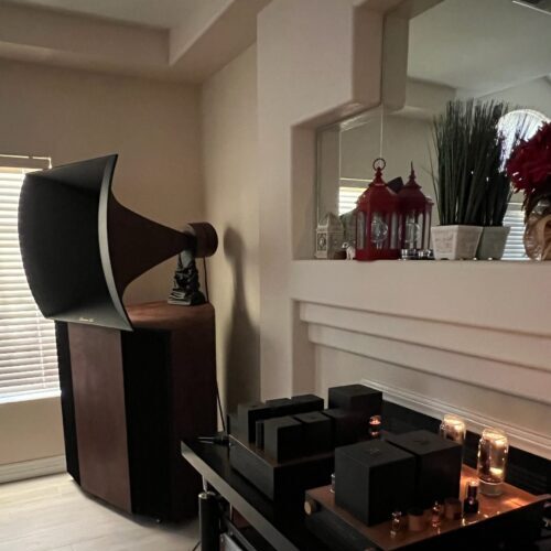 A Vista 3-Way Horn Speaker is on the left, while a shelf displaying audio equipment with glowing vacuum tubes is in the foreground. Decor items adorn a mantel in the background.