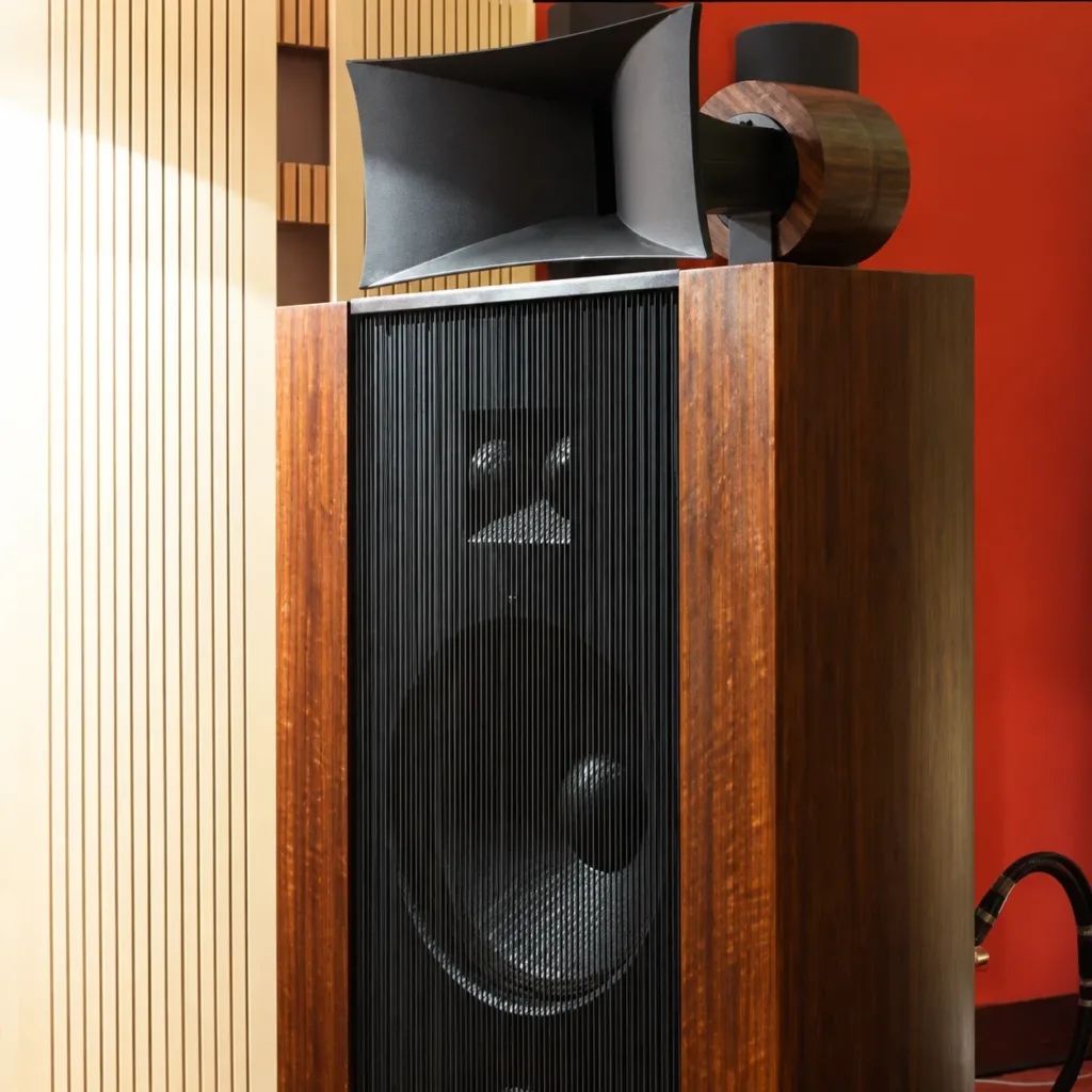 Tall, black textured Vista 3-Way Horn Speakers with reflective surfaces, displayed against a backdrop of red and wooden panels, resembling a field coil amplifier.