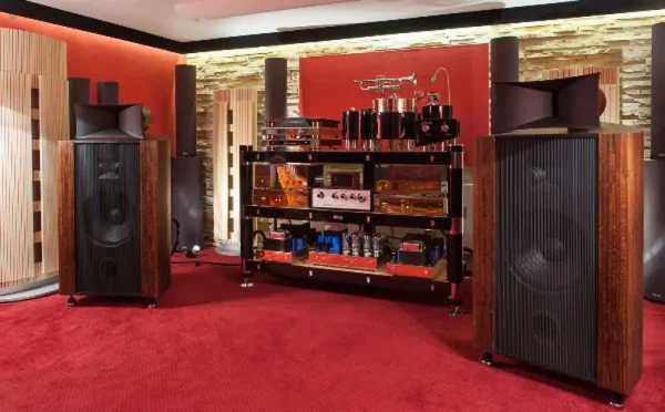 A high-end audio room with large Vista 3-Way Horn Speakers, an amplifier rack with various audio components including a preamplifier, and stone accent walls.