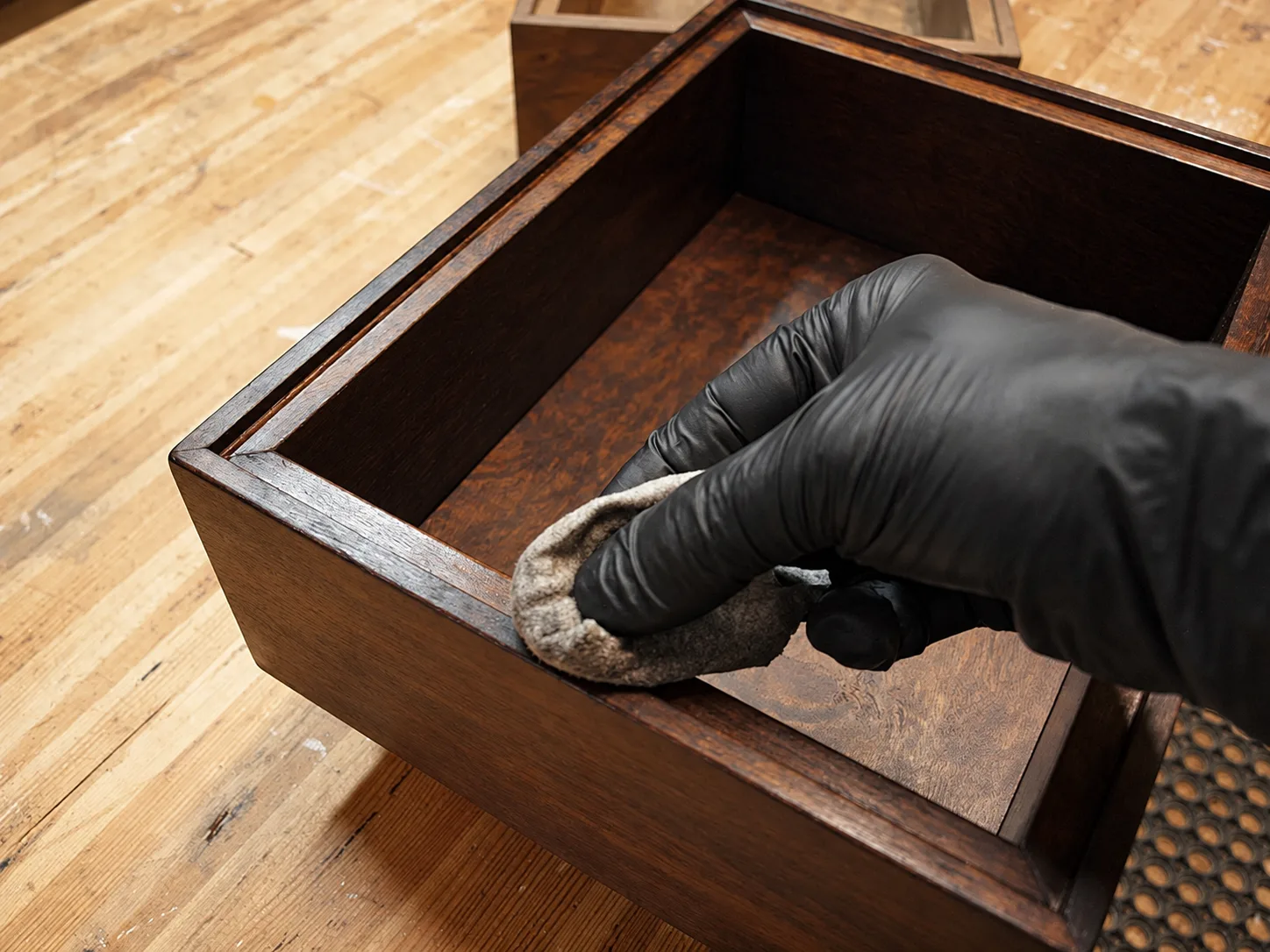 A gloved hand working finish into the burl veneer inside an open amplifier cabinet.