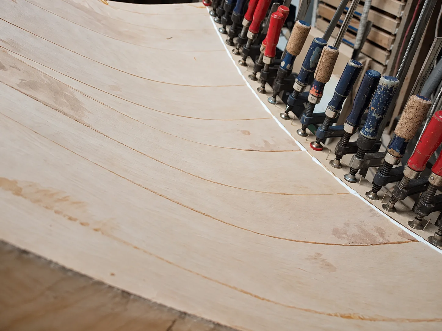 A laminated horn curve held under a long row of hand screw clamps while the glue sets.