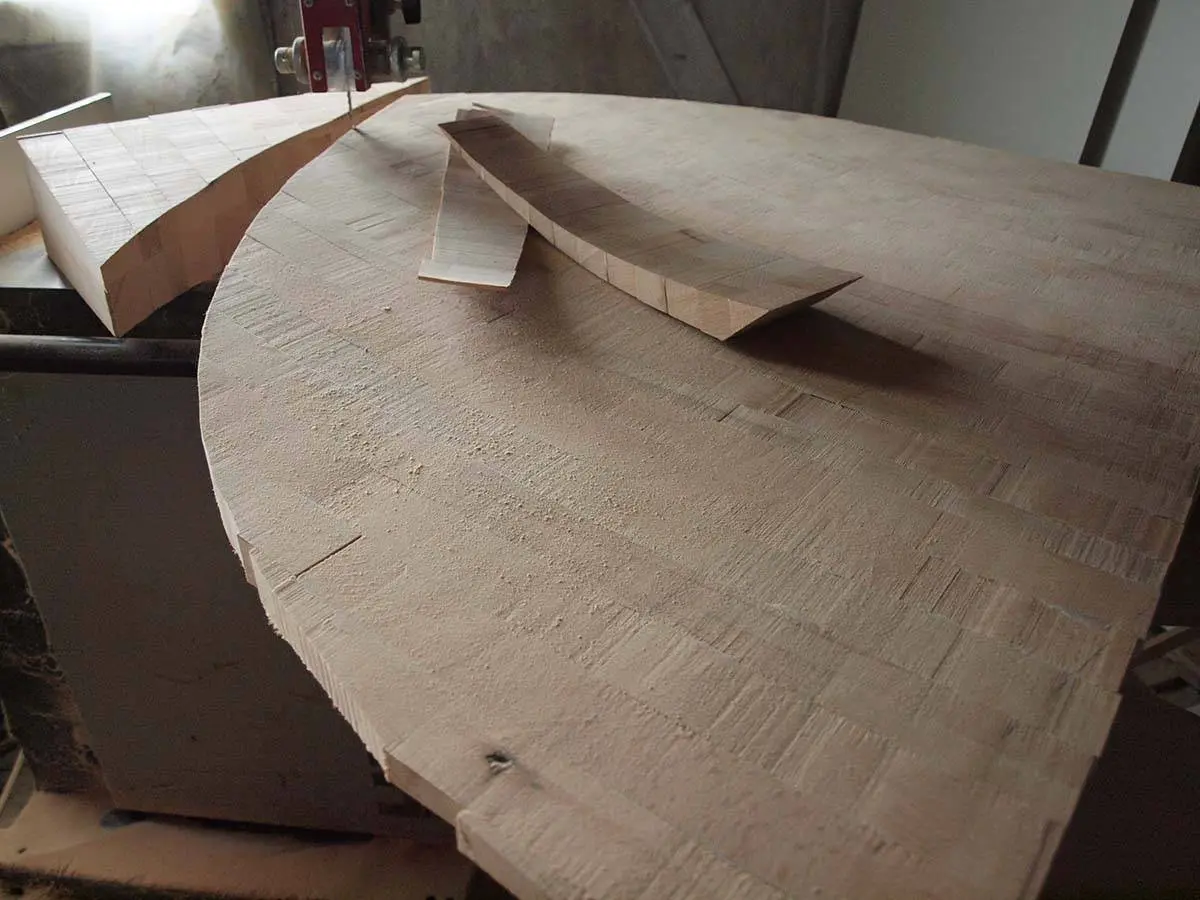 A large round end-grain wood plate on a band saw with a cut curved strip lying on it