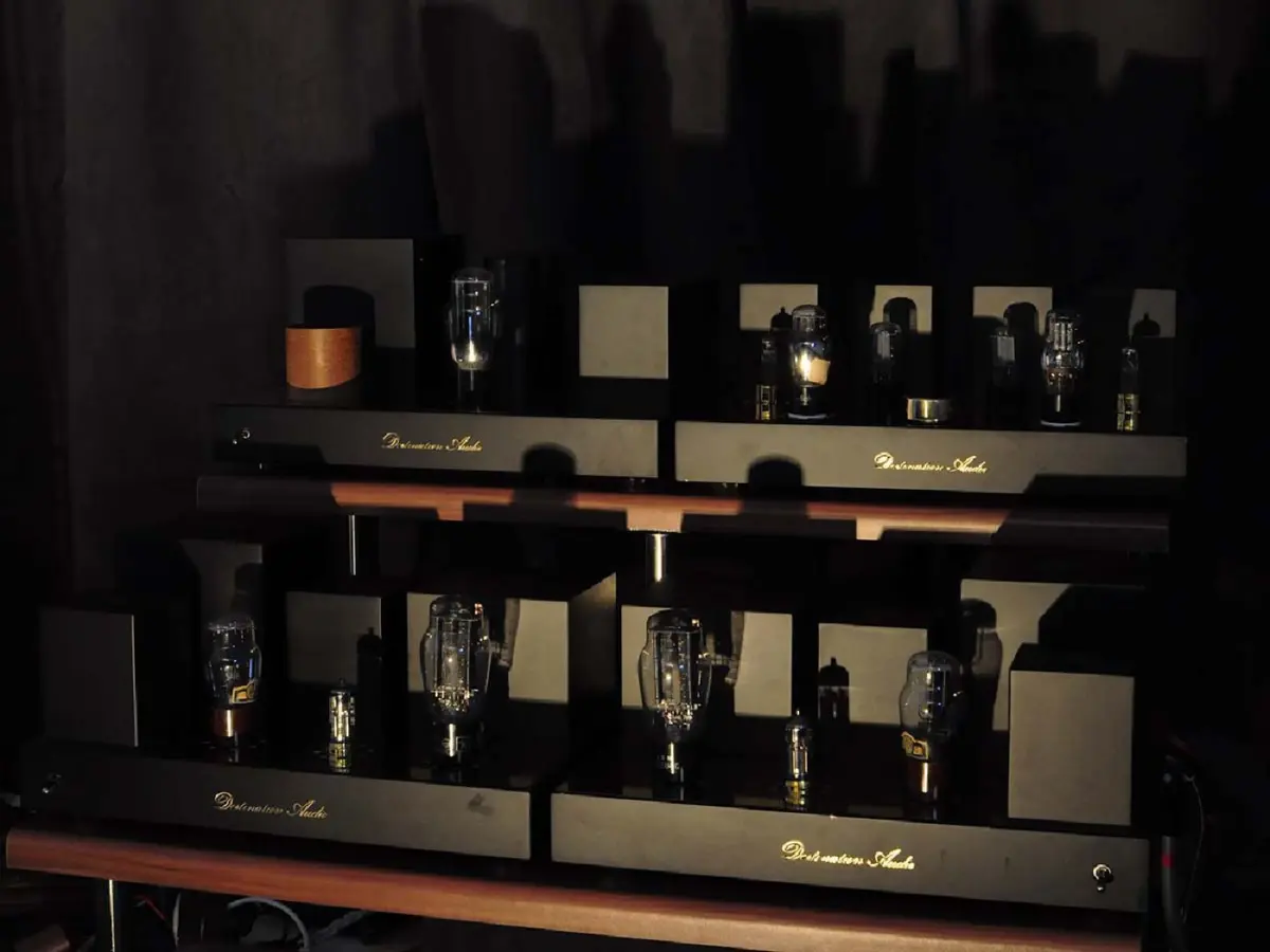 Four Destination Audio tube amplifiers on a two-shelf rack in a dim room